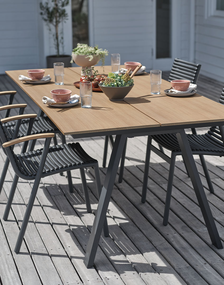 Outdoor-Tisch mit Tischplatte aus Kunstholz und stapelbaren Kunststoffstühlen mit Armlehnen aus Teakholz