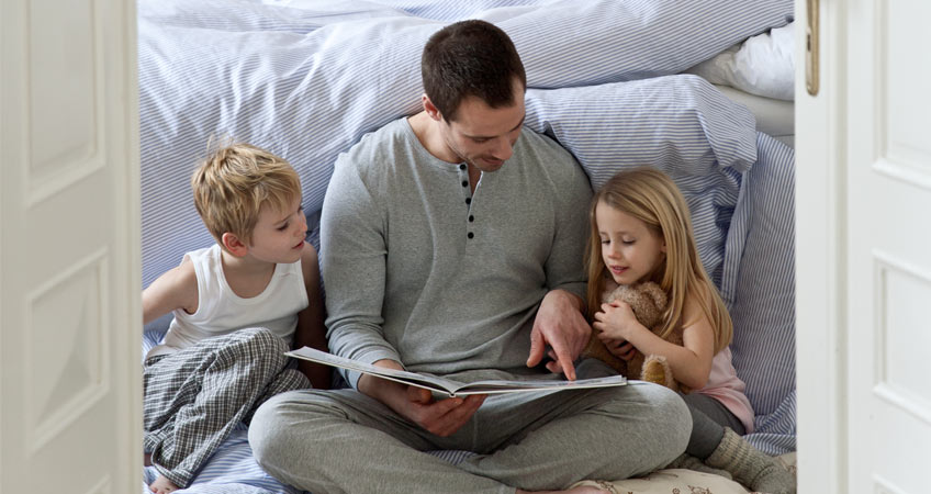 Vater liest seinen 2 Kindern eine Gute-Nacht-Geschichte vor